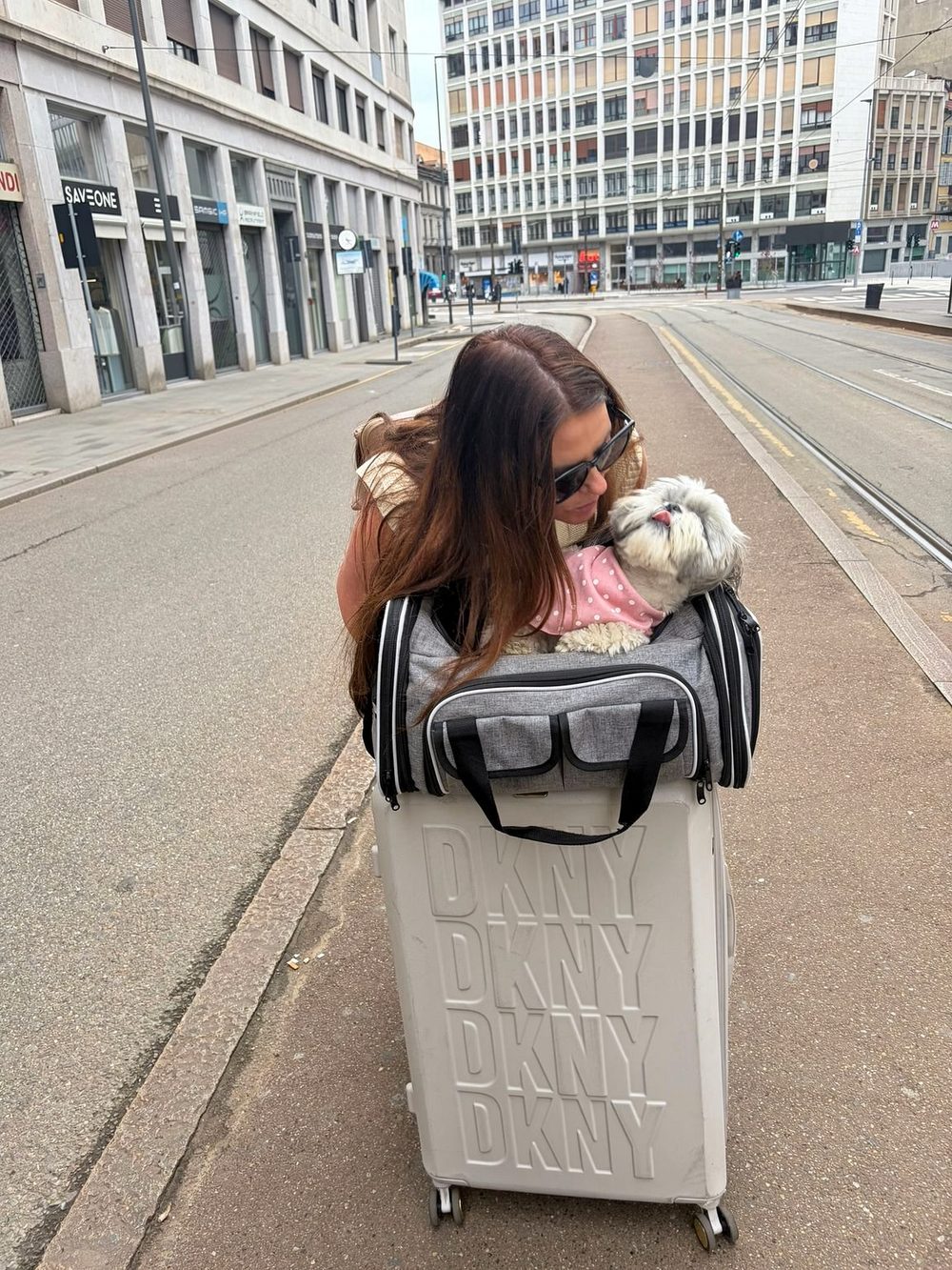 Pam leaning in to Daisy the Shih Tzu, who is sitting in her grey cabin carrier on top of a suitcase